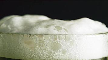 Beer glass with overflowing foam. Beer is pouring into glass on the wooden table, dark background.