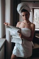 hermosa joven en una toalla fuma un cigarrillo y lee el periódico