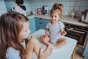 Two little girls in the kitchen sitting on the table. photo