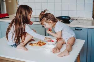 Two little girls in the kitchen sitting on the table. photo