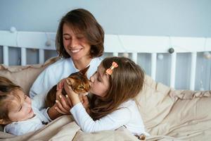 Happy mother and two daughters smiling hugs in bed photo