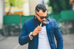 hombre con barba fuma cigarrillo electrónico foto