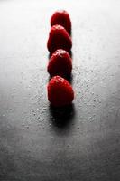 Red raspberries in a row with sugar on top on a black griddle. Backlighting. Vertical image. photo