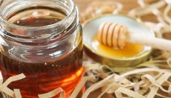 Honey in glass jar with blurred honey dipper in background. Health and beauty product sustainable lifestyle concept. photo