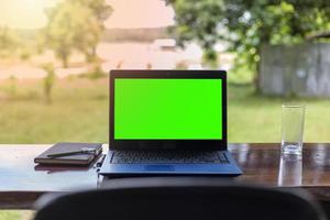 cuaderno de pantalla verde con cuadernos colocados sobre una mesa de madera contra un hermoso paisaje natural. foto