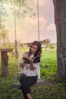 A beautiful woman sits on a swing and writes down something in a notebook with love. photo