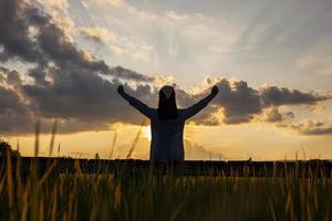 Behind the shadow of a woman sitting on a wooden walkway beside a field. waving joyfully in the setting sun photo