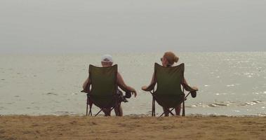 duas meninas estão sentadas em espreguiçadeiras na margem de uma praia vazia perto da água video