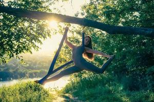 A young gymnast is engaged in aerial yoga in nature in the park, using a combination of traditional yoga poses, pilates and gentle dance photo
