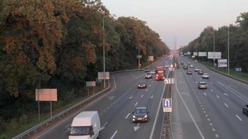 coches en movimiento en la autopista durante la puesta de sol. tráfico intenso en una autopista o carretera, vista superior de la carretera. los rayos dorados del sol vespertino iluminan el transporte. ucrania, Kyiv - 3 de octubre de 2021. video