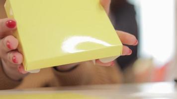 een onherkenbaar vrouw vouwen een klein geel karton doos. productie van karton dozen van papier. verpakking fabricage bedrijf. detailopname van handen aan het doen papier ambachten Bij een creatief les. video