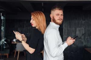 los jóvenes se paran de espaldas entre sí con un teléfono inteligente en las manos. foto