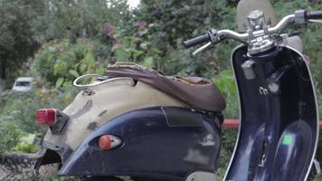 wijnoogst haveloos scooter of mini motorfiets staat buitenshuis. populair mode van vervoer. de stuurinrichting wiel van een oud blauw bromfiets met een bruin stoel. video