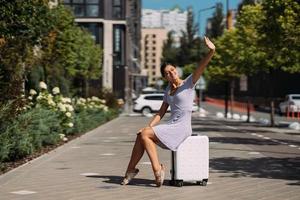 Pretty young woman sits on suitcase outside. photo