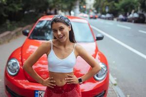 Portrait of pretty Caucasian woman standing against new red car photo