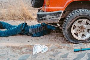 man lies under a 4x4 car on a dirt road photo