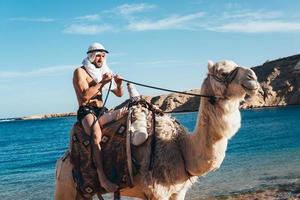 Guy rides on a camel on the beach photo