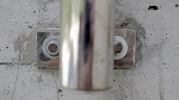 parafuso no close up macro do muro de cimento filme. fixação de um tubo de trilho cromado com parafusos a uma parede de concreto. parafuso aparafusado no concreto ao lado de outros parafusos. cinza metálico.