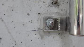 Bolt in concrete wall macro closeup stock footage. Fastening a chrome-plated railing pipe with bolts to a concrete wall. Bolt Screwed into concrete next to other bolts. Gray metallic. video