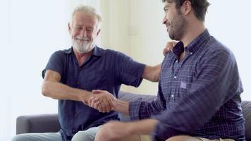 Happy family with senior father talking with son and handshake together with cheerful on sofa, young man conversation and hug with elderly for resting on couch in the living room, lifestyle concept. video