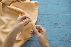 vista superior de la mano del sastre reparar un pantalón amarillo sobre fondo de mesa azul foto