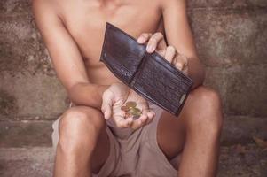 hombre sentado frente a la vieja pared de ladrillos y sosteniendo una billetera vacía foto