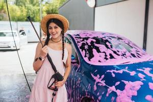 Woman with hose stands by car covered in pink foam photo