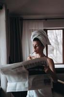 Beautiful young woman in a towel smokes a cigarette and reads newspaper photo