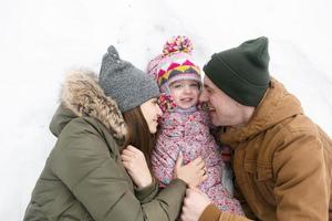 papá, mamá y su pequeña hija yacen en la nieve foto