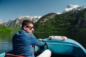 Handsome young guy controls a motorboat on a mountain lake photo