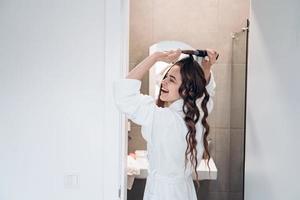 bella mujer sonriente rizando el cabello largo con rizador. foto