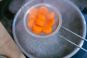 The image of a small amount of chopped carrots over a boiling pan photo