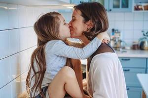 mamá besa a su pequeña hija en la cocina foto