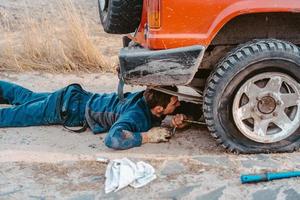 el hombre yace debajo de un camión 4x4 en un camino de tierra foto