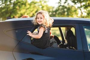 A little girl is sitting on the door of the car photo