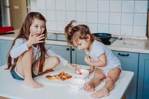 Two little girls in the kitchen sitting on the table. photo