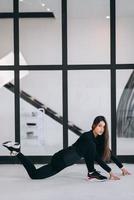 Young female wearing black sports suit exercising yoga pose indoors. photo