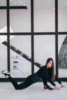 mujer joven con traje deportivo negro haciendo pose de yoga en el interior. foto