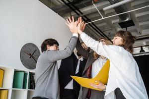 Cheerful young group of people standing in the office and giving high five photo