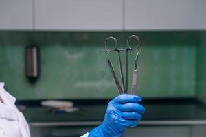 A rubber gloved hand holds two scalpels and a clamp photo
