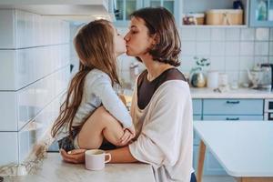 Mom kisses her little daughter in the kitchen photo