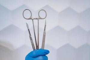 A rubber gloved hand holds two scalpels and a clamp photo