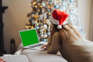 Female wearing santa hat while speaking with online friend on laptop photo