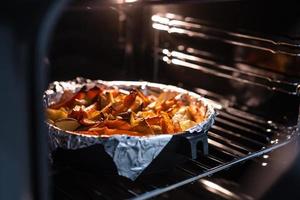 Baked potatoes with carrot and other spices in roasting pan. photo