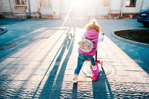 Little girl with blonde hair rides on scooter photo