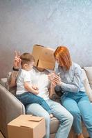 Young happy family with kid unpacking boxes together sitting on sofa photo