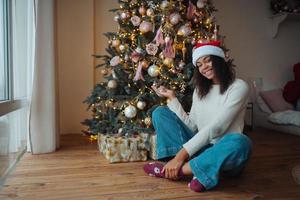 linda mujer afroamericana se sienta cerca de un árbol de navidad foto