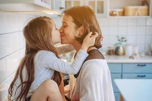 Mom kisses her little daughter in the kitchen photo