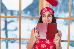 Beautiful young brunette woman wearing red pajamas sitting home by the window photo