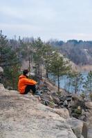 A young man sitting on the edge of a cliff poses for the camera photo